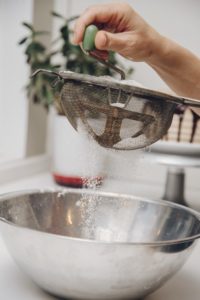 Baker sifting flour through metal sieve